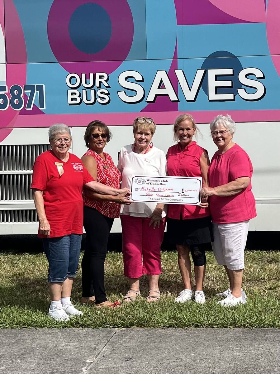 Five members in red club shirts hand a check to Michelle-O-Gram in front of the Our Bus Saves mammography bus